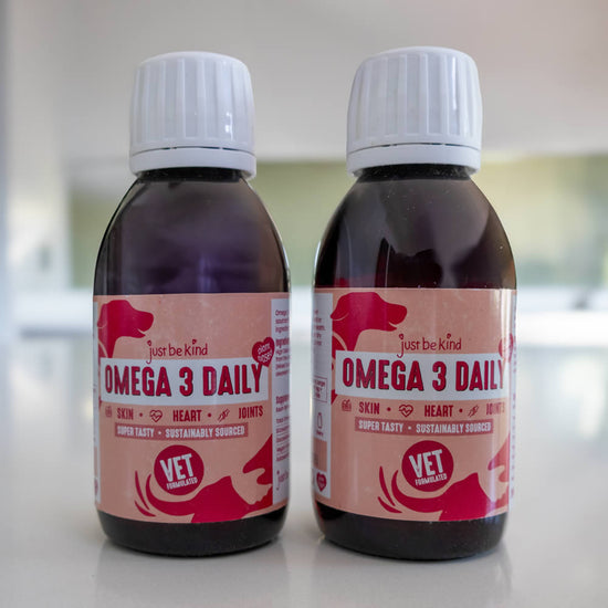 Two bottles of 'Just Be Kind Omega 3 Daily' supplement for pets on kitchen surface