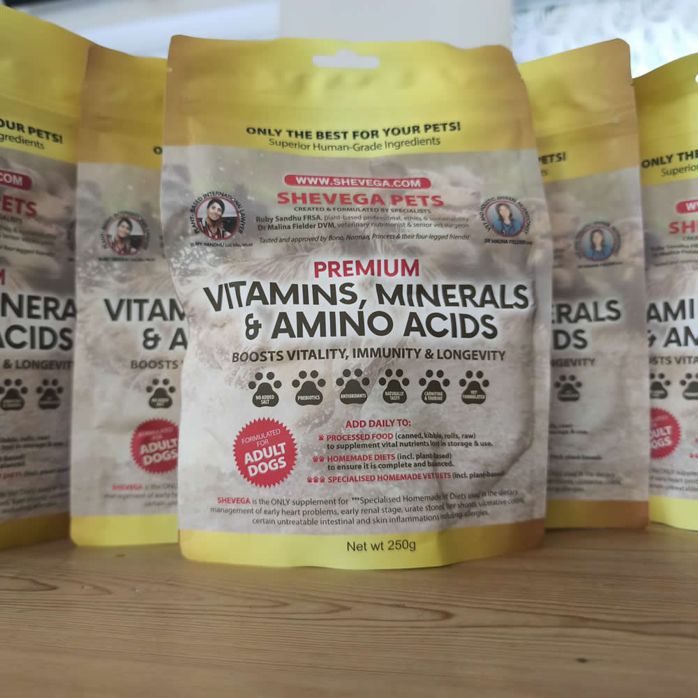 A 250g bag of Shevega Pets Premium Vitamins, Minerals & Amino Acids for adult dogs, displayed on a wooden surface with other bags in the background.
